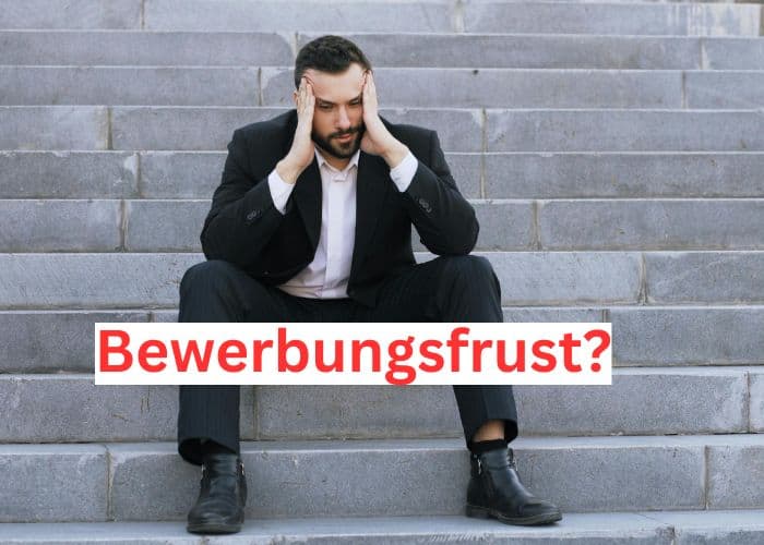 Ein Mann im Anzug sitzt auf einer Freitreppe und stützt seinen Kopf gestresst in die Hände. Das deutsche Wort "Bewerbungsfrust?" (Bewerbungsfrust) steht in fetten roten Buchstaben quer über das Bild geschrieben.