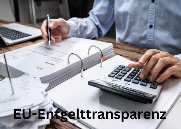 Eine Person prüft Dokumente und benutzt einen Taschenrechner an einem Schreibtisch mit verstreuten Papieren und einem Laptop. Der deutsche Text EU-Entgelttransparenz erscheint am unteren Rand des Bildes.