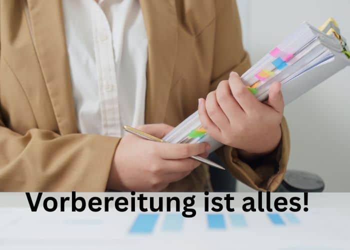 Eine Person in einem braunen Blazer, die eine Mappe mit bunten Registerstreifen in der Hand h&auml;lt; &uuml;ber dem Bild steht auf Deutsch &bdquo;Vorbereitung ist alles!&ldquo;, was auf Englisch &bdquo;Preparation is everything!&ldquo; bedeutet.