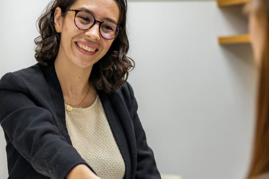 Eine Frau in Business-Kleidung lächelt und gibt während eines Vorstellungsgesprächs die Hand. Der Text darüber lautet: 12 Tipps zur Jobsuche von einer ehemaligen Personalvermittlerin.
