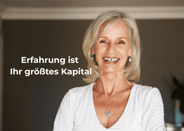Eine lächelnde ältere Frau mit weißblondem Haar steht in einem Raum. Der deutsche Text lautet: „Erfahrung ist Ihr größtes Kapital“. Sie trägt ein weißes Oberteil und eine Halskette mit Anhänger.